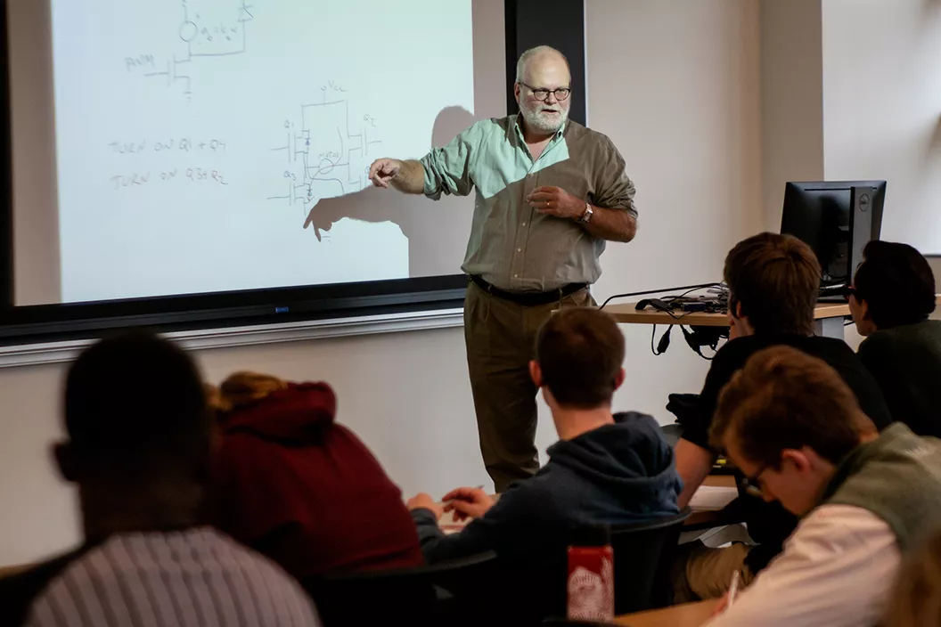 Professor stands in front of screen and presents to class in engineering course