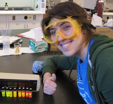 Althea Gaffney, smiling and wearing safety goggles,  gives a thumbs up for chemistry