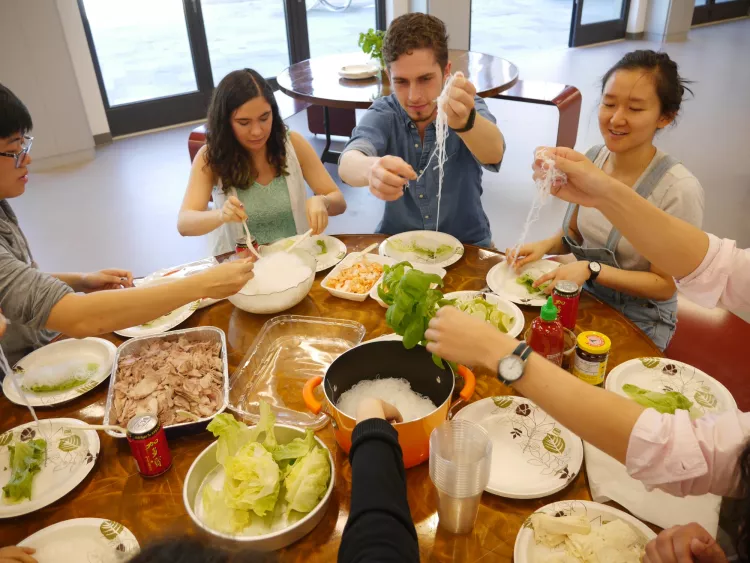 A group of students enjoying what appears to be a meal consisting of Vietnamese vermicelli noodles and some leafy greens