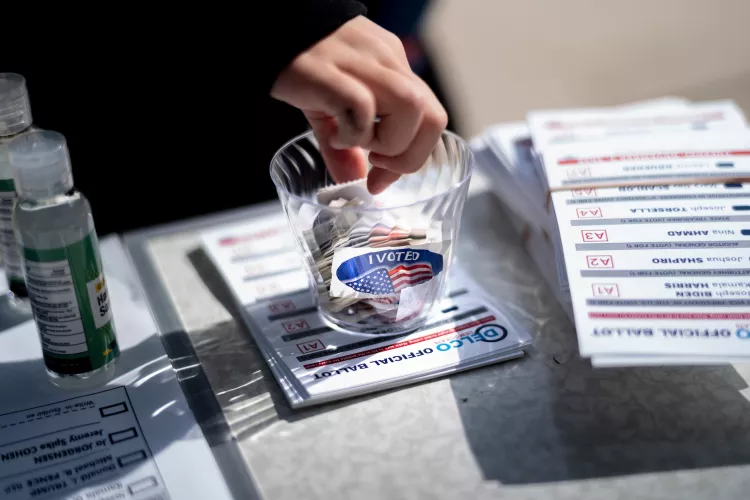 Person's hand reaches into cup with voting stickers