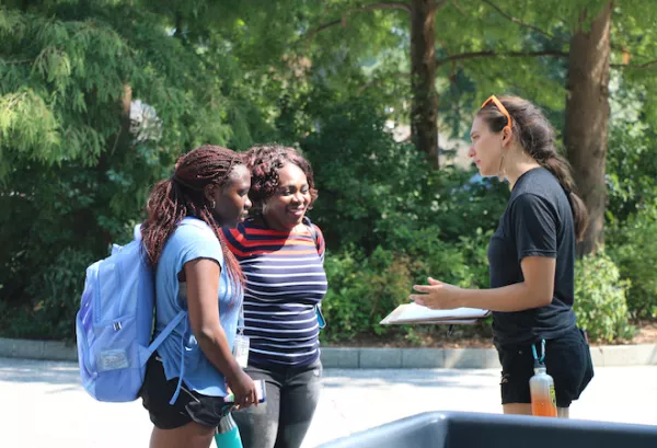 Two people standing outside talk to a person holding a clipboard