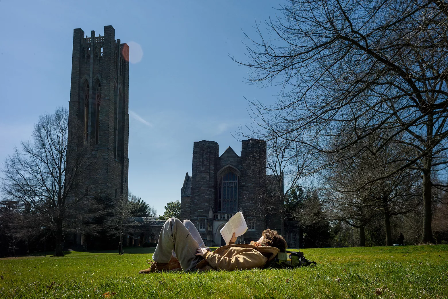 Student lies on ground and reads book outdoors